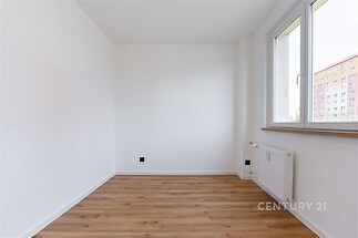 Světlý pokoj s parketovou podlahou, velkými okny a moderními bílými stěnami nabízí prostor pro flexibilní využití.
