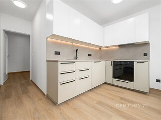 Moderní kuchyň s parketovou podlahou a vestavěnými spotřebiči, bílá dvířka skříněk a dekorativní osvětlení pod linkou dodávají elegantní vzhled.