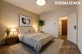 Prostorná ložnice s parketovou podlahou, moderním osvětlením a velkou rostlinou, nabízí klidnou atmosféru a stylový design.