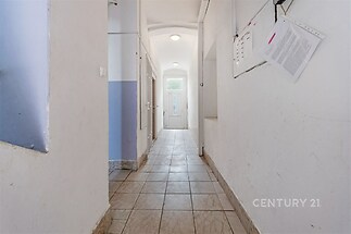 Úzká chodba, dlažba, bílá stěna, rekonstrukce, přírodní světlo, jednoduché osvětlení.