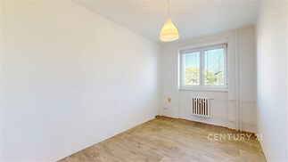 Prázdný pokoj s parketovou podlahou, velkým oknem a bílými stěnami nabízí světlý prostor vhodný pro různé využití.