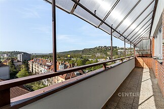 Prostorný balkon s dlažbou a krytým zastřešením nabízí panoramatický výhled na okolní krajinu a městské prostředí