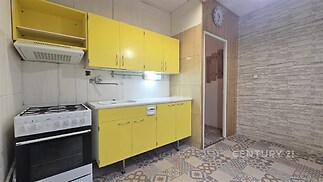 Kuchyň s retro žlutými skříněmi, vzorovanou dlažbou a plynovým sporákem, evokuje vintage styl a nabízí prostorný úložný prostor.