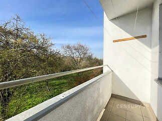 Balkon s dlažbou, která poskytuje klidný výhled na zahradu, ideální pro relaxaci. Vnější bílá stěna a dostatek prostoru pro venkovní posezení.