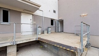 Průmyslový nakládací prostor s betonovým pódium, kovovým zábradlím a přístupovými dveřmi, využitelný pro komerční účely.