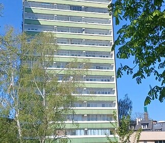Vysoká bytová budova v moderním stylu s velkými okny, obklopená zelení, světlá fasáda poskytuje čistý vzhled