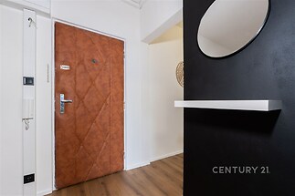 Vstupní chodba s dřevěnou podlahou, moderní černou stěnou a kulatým zrcadlem, dveře s koženým čalouněním, stylový interiér.