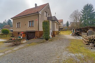 Rodinný dům s červenou sedlovou střechou, prostorný dvůr, dřevěná terasa, klidná lokalita, částečně zrekonstruovaná fasáda.