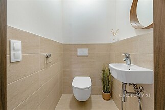 Moderní toaleta s dlažbou, světlá omítka, bílé keramické umyvadlo, závěsné WC, minimalistický styl, elegantní příslušenství.