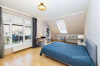 Prostorná ložnice s parketovou podlahou, velkými okny a moderním zařízením, včetně pracovní plochy a světlého interiéru.