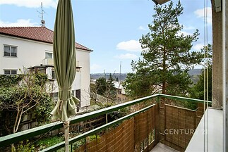 Balkón s krásným výhledem, prostorný a vhodný pro relaxaci, disponuje dlážděnou podlahou, zeleným zábradlím a je ideální pro venkovní posezení.