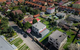 Letecký pohled na klidnou rezidenční čtvrť s moderními rodinnými domy, zahradami a dlážděnými příjezdovými cestami.