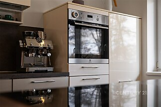 Moderní kuchyň s lesklou pracovní deskou, vestavěnou troubou a kávovarem, světlý design elegantně doplněn o nerezové spotřebiče.