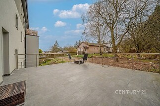 Prostorná terasa s dlažbou, výhledem na zahradu a kovovým zábradlím, ideální pro posezení venku, moderní styl s přírodním okolím