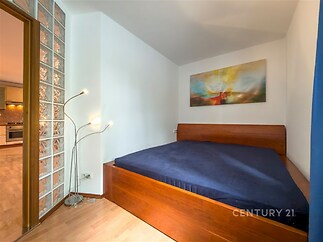 Ložnice s dřevěnou postelí, moderní parketovou podlahou a skleněnou příčkou. Světlý a stylový prostor s uměleckým obrazem na stěně.