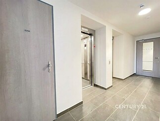 Chodba s moderním výtahem, dlažbou a dřevěnými dveřmi, světlý prostor v rekonstruovaném domě, klidné a bezpečné prostředí.