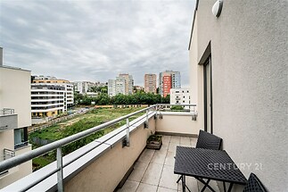 Moderní balkon s dlažbou a výhledem na městskou zástavbu, vybavený elegantním zahradním nábytkem, ideální pro relaxaci