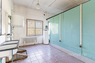 Průmyslová kuchyň s dlažbou, velká okna a úložné skříně, potřebuje rekonstrukci, slunný a vzdušný prostor vhodný pro modernizaci.