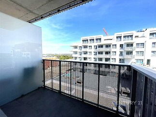 Balkon s moderní dlažbou a kovovým zábradlím, nabízí výhled na rekonstruovaný bytový dům.