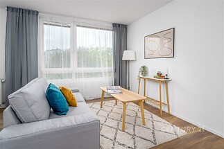 Světlý obývací pokoj, parketová podlaha, velká okna, moderní design, minimalistický nábytek, elegantní a útulný prostor.