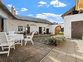 Venkovní dvorek s dlažbou, rustikálními prvky a dřevěným nábytkem, zděné zdi, prostorný s příjemným venkovským nádechem.