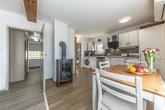 Moderní kuchyň s parketovou podlahou a krbovými kamny, bílý nábytek a velká okna poskytují světlý a prostorný pocit.