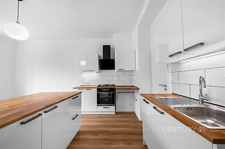 Moderní kuchyň s dřevěnou pracovní deskou, bílými skříňkami a světle hnědou parketovou podlahou, vybavená vestavěnými spotřebiči.