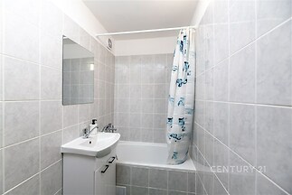 Koupelna s dlažbou a vanou, moderní umyvadlovou skříňkou, neutrálními tóny a závěsem, vhodná pro menší byt nebo rekonstrukci.