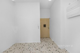 Prázdná vstupní hala s teracovou dlažbou, bílými stěnami a dveřmi v nájemním domě.