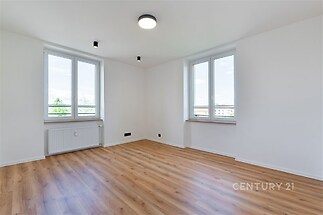 Světlý obývací pokoj s parketovou podlahou, velkými okny a moderním osvětlením v rekonstruovaném bytě.