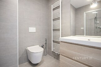 Moderní koupelna s šedou dlažbou, závěsnou toaletou a dřevěným umyvadlovým pultem, doplněná otopným žebříkem a sprchovým koutem.