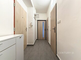 Úzká vstupní chodba s dlažbou, světlé stěny, moderní dveře z světlého dřeva, vestavěná skříň a úložný prostor, čistý a udržovaný prostor.