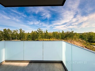 Světlý balkon s moderní dlažbou, skleněným zábradlím a výhledem na les, ideální pro relaxaci v přírodní atmosféře.