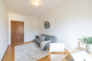 Světlý obývací pokoj s parketovou podlahou, moderní sedačkou a velkým kobercem, nabízí útulný prostor a elegantní design.