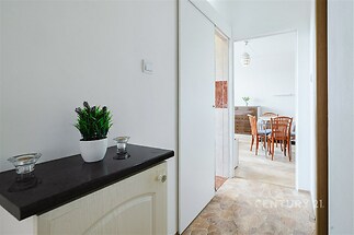 Úzká chodba s dlažbou a světlými stěnami, přecházející do světlé jídelny s dřevěným nábytkem, oddělená posuvnými dveřmi.