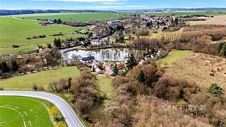 Jezero obklopené zelení a vesnickými domy, venkovský styl, klidná přírodní oblast, ideální pro rekreaci a relaxaci.