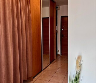 Chodba s dlažbou, vestavěné skříně, moderní osvětlení, závěsy v teplých tónech, útulný interiér.