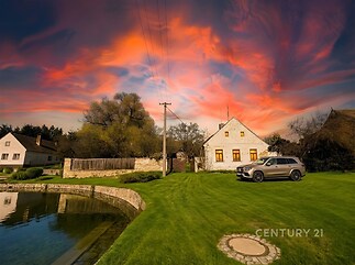 Kamenný venkovský dům s moderním autem na prostorné zelené zahradě, vedle rybníka. Okolí nabízí klid a přírodní krásy.