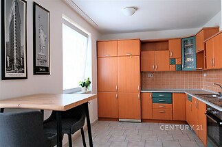 Kuchyň s dlažbou, dřevěnými skříňkami a moderním stylem, velké okno poskytuje dostatek světla.