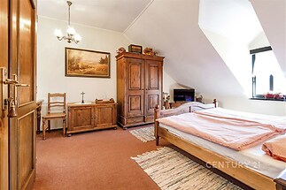 Útulná ložnice s dřevěným nábytkem, šikmým stropem a kobercem ve venkovském stylu, ideální pro klidný odpočinek.