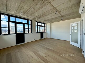 Průmyslový obývací pokoj s dřevěnou parketovou podlahou a betonovým stropem nabízí velká okna s panoramatickým výhledem na město