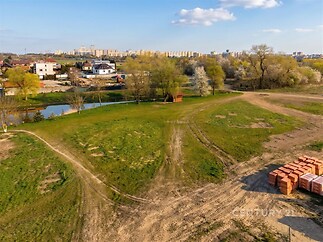 Prázdný stavební pozemek s travnatou plochou, okolní příroda a blízkost města, ideální pro stavbu moderního rodinného domu.