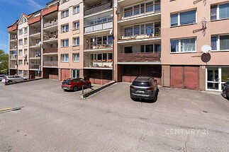 Parkoviště u bytového domu s asfaltovým povrchem, přístup k vchodům a garážím, moderní městský styl, udržovaný stav