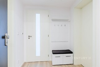 Vstupní hala s parketovou podlahou, moderní bílý interiér, nástěnný věšák a úložná lavice.