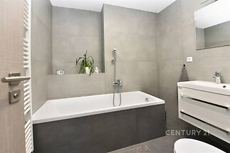 Moderní koupelna s dlažbou, elegantní vanou a nástěnným umyvadlem, světlá a prostorná atmosféra, ideální pro relaxaci.