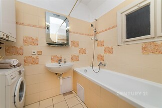 Koupelna s keramickou dlažbou, moderním umyvadlem a vanou, světlé obklady s dekorem, plynový kotel, malá okna zajišťující přístup denního světla.