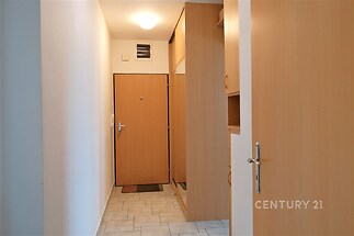 Úzká vstupní chodba, světlé dlažby, vestavěné skříně z dřeva, moderní osvětlení, čisté stěny, dřevěné interiérové dveře.