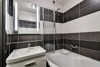 Moderní koupelna s vanou, sprchovým koutem a dlažbou v černobílé kombinaci, elegantní osvětlení, dobře udržovaná a světlá.