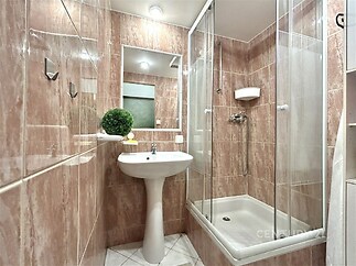 Kompaktní koupelna s dlažbou v imitaci kamene, sprchový kout a bílé sanitární zařízení, moderní osvětlení a zrcadlová stěna