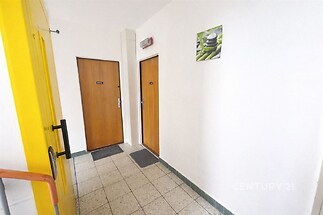 Společná chodba s dlažbou, bílými stěnami a dřevěnými dveřmi, moderní design vhodný pro bytový dům.